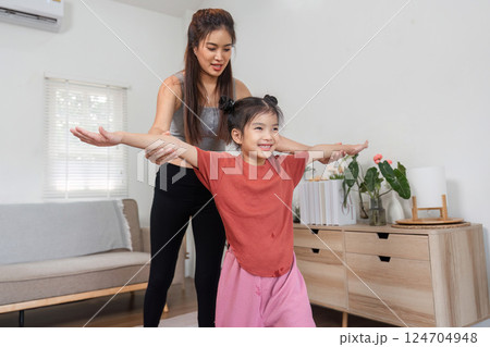 Exercise and Fitness Fun. A guiding mother helping her daughter with a stretching workout in a cozy living space. 124704948
