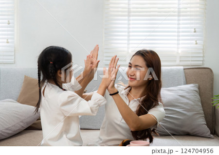 Playful Interaction and Bonding. A mother and daughter playing a hand game at home, fostering joy and connection. 124704956