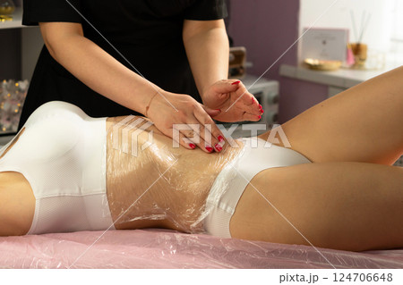 Beautician uses rhythmic hand motion on client's wrapped midsection. Beautician uses rhythmic hand motion on client's wrapped midsection. 124706648