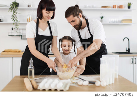 Caucasian family including father, mother, and daughter cooking in modern kitchen kneading dough. Family bond and home baking activity emphasizing togetherness. Caucasian family including father, mother, and daughter cooking in modern kitchen kneading dough. Family bond and home baking activity emphasizing togetherness. 124707405