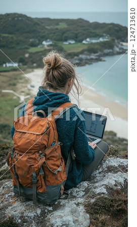 Remote work inspiration: woman with laptop on scenic clifftop overlooking coastal landscape 124713610