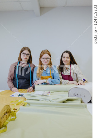 Three female seamstresses and fashion designers are standing at a table with a roll of fabric 124715233