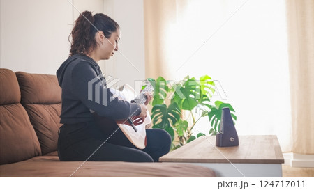 Young woman playing acoustic guitar at home using a metronome 124717011