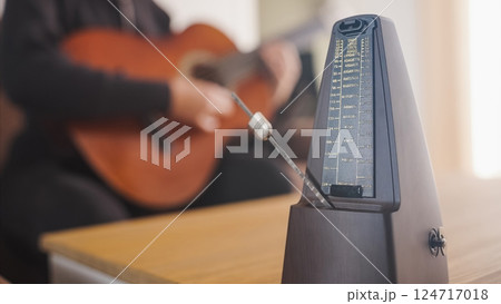 Musician practicing guitar using traditional metronome for rhythm Musician practicing guitar using traditional metronome for rhythm 124717018