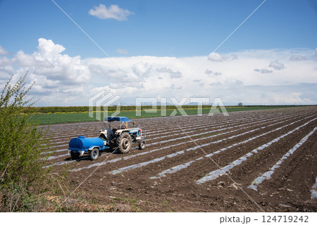 Blue tractor on the field and carries barrel for watering field. Blue tractor on the field and carries barrel for watering field. 124719242