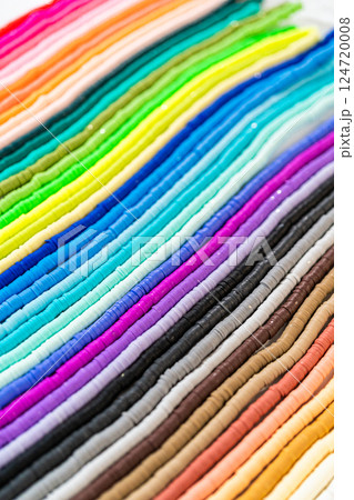 A vibrant collection of clay beads, neatly arranged by color on a white table, ready to inspire young crafters to create their own unique bracelets. 124720008