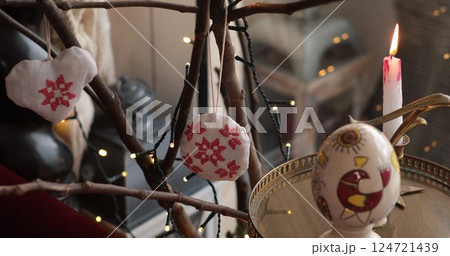 Easter handcrafted decorations displayed on a branch with warm candlelight illuminating the vibrant colors and intricate designs, creating a festive atmosphere in a cozy indoor setting Easter handcrafted decorations displayed on a branch with warm candlelight illuminating the vibrant colors and intricate designs, creating a festive atmosphere in a cozy indoor setting 124721439