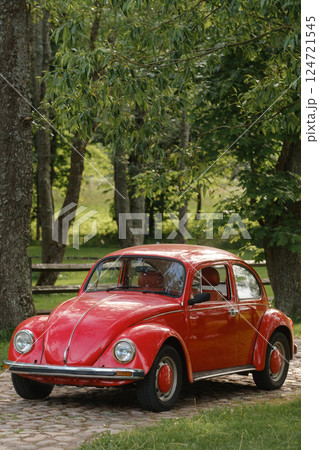 Classic red car parked under lush trees in a serene rural setting during daylight hours 124721545