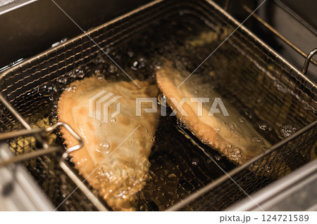 Crispy empanadas frying in hot oil in a restaurant kitchen during a busy evening service 124721589