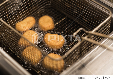 Golden brown chicken nuggets frying in hot oil in a kitchen setting during lunchtime, showcasing a tasty snack preparation 124721607