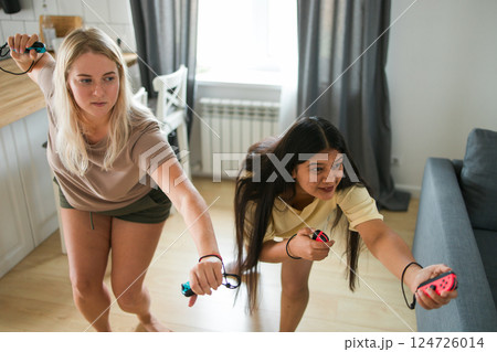 Friends having fun with drinks and snacks while playing video game at home. Two men playing video game holding joysticks while another man holds a mobile phone in hand. 124726014