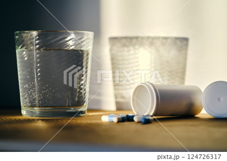 A glass of water and a bottle of pills in the sunlight. 124726317