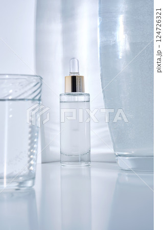 Bottle with serum on a white background with glare from water. Bottle with serum on a white background with glare from water. 124726321