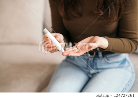 Young woman checking blood sugar level with glucometer at home, monitoring diabetes health on the couch. 124727261