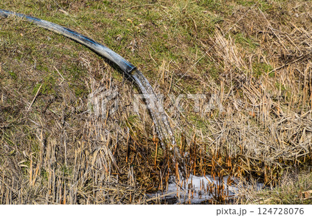 Water flows out of the hose into the ditch 124728076