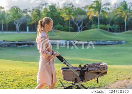 Mother walking with her baby in a stroller in the park. Peaceful outdoor bonding time. Parenthood, baby care, and family lifestyle concept 124728190
