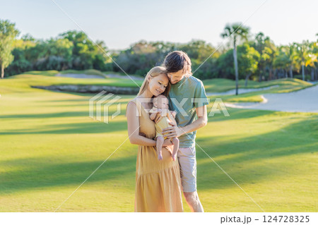 Loving parents with their newborn baby on a meadow in the park. Happy family enjoying nature, bonding, and peaceful outdoor moments. Parenthood, love, and family connection concept 124728325