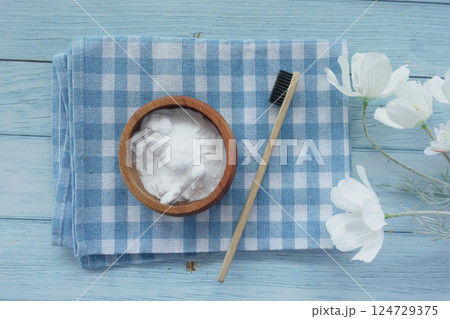 A wooden bowl of baking soda, a bamboo toothbrush, and a glass jar on a fabric 124729375