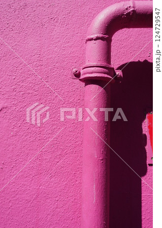 Pink wall with pipe, illuminated by sun, displaying modern urban design with vibrant colors 124729547