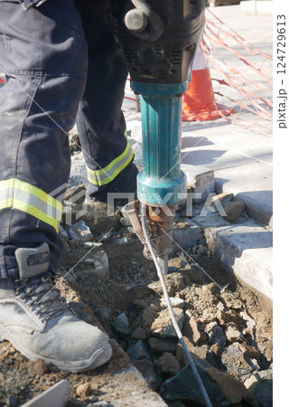 Construction worker using jackhammer on pavement in a city area 124729613