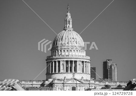 The iconic dome of St. Paul's Cathedral rises majestically against a clear sky, showcasing its architectural beauty. Surrounding buildings contrast with its historic elegance. 124729728