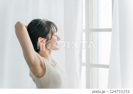 寝起き・起床時にカーテンの前で朝日を浴びる女性（脱毛・脇） 124731252