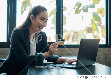 Smiling businesswoman using a credit card for online shopping on a laptop in a bright, modern office. Smiling businesswoman using a credit card for online shopping on a laptop in a bright, modern office. 124734878