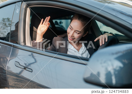 Confident businesswoman in a car, smiling and showing an OK gesture, symbolizing success and positivity in a modern urban environment. 124734883
