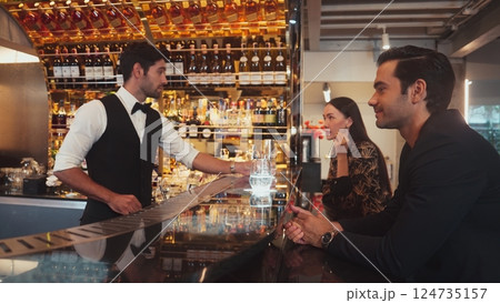 Focusing smiling smart bartender serving soda to customer couple. Vinosity. 124735157