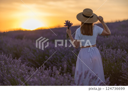 A woman stands in a field of lavender flowers, holding a bouquet of flowers 124736699