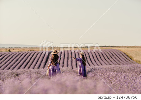 Mom and daughter are running through a lavender field dressed in purple dresses, long hair flowing and wearing hats. The field is full of purple flowers and the sky is clear. Mom and daughter are running through a lavender field dressed in purple dresses, long hair flowing and wearing hats. The field is full of purple flowers and the sky is clear. 124736750