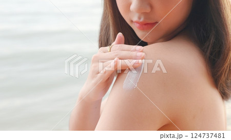 Beautiful Asian woman applying sun protection cream on tanned shoulder on the beach, sun Cream, Close up female in bikini using sunscreen lotion on back body before sunbathing 124737481