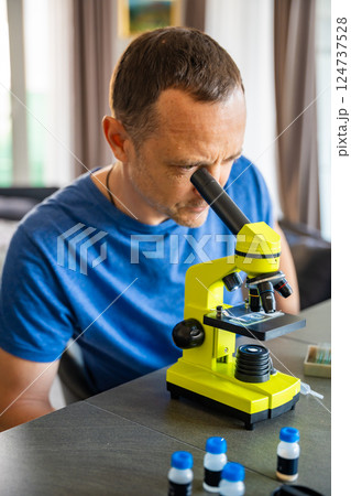 Man examining various samples under a microscope at home as a hobby. Concept of scientific curiosity and amateur microscopy 124737528