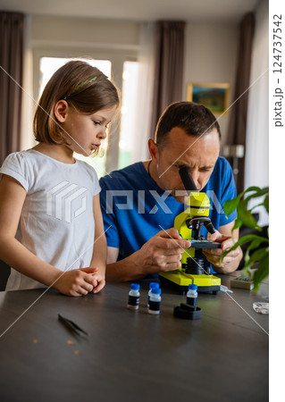 Father and daughter examining various plant samples under a microscope at home. Concept of family science education and botanical exploration Father and daughter examining various plant samples under a microscope at home. Concept of family science education and botanical exploration 124737542