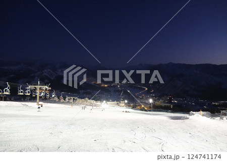 ナイター照明で白く反射するゲレンデと深い青空にうっすらと見える山の稜線 124741174
