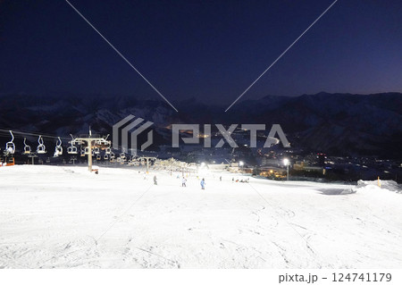 ナイター照明で白く反射するゲレンデと深い青空にうっすらと見える山の稜線 124741179