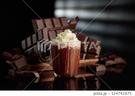 A mug of hot chocolate with whipped cream against broken bitter chocolate bars. A mug of hot chocolate with whipped cream against broken bitter chocolate bars. 124742875
