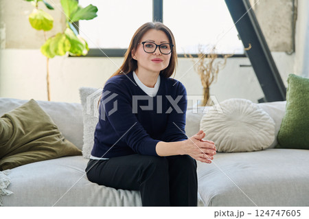 Portrait of beautiful middle aged smiling woman sitting at home on sofa 124747605
