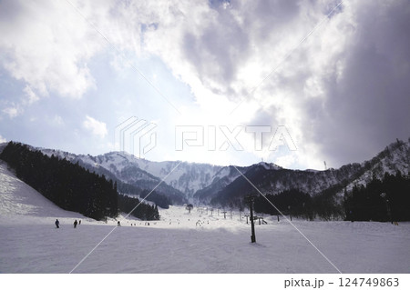 厚い雲の切れ目から青空が見えゲレンデのスロープを太陽が照らす 厚い雲の切れ目から青空が見えゲレンデのスロープを太陽が照らす 124749863