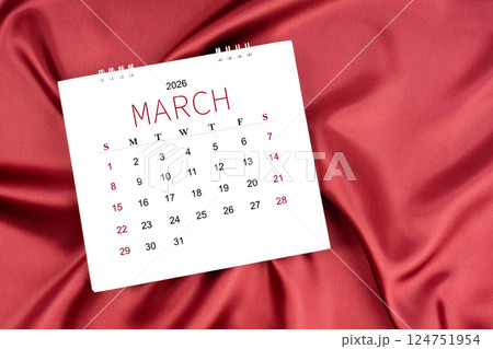 March 2026 Monthly desk calendar on red silk textile background. 124751954