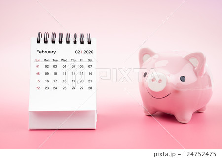 Desk calendar for February 2026 and pink piggy bank on pink background. 124752475