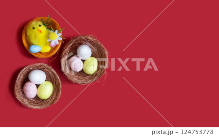 Lots of Easter eggs and a toy chicken in nests on a red background. Easter concept, close-up. Lots of Easter eggs and a toy chicken in nests on a red background. Easter concept, close-up. 124753778