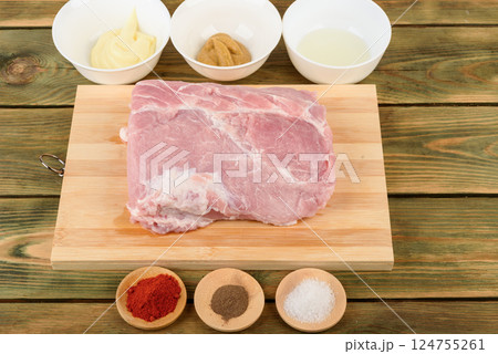 Raw pork meat on a cutting board and bowls with spices for marinade. 124755261