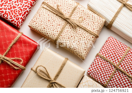 presents arranged in a balanced composition, wrapped in red and beige paper with intricate festive patterns, adorned with satin ribbons and rustic twine, soft diffused lighting highlighting textures 124756921