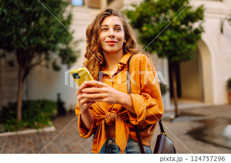 Portrait of a young woman holding a phone in her hands on a city avenue, on a sunny day. 124757296