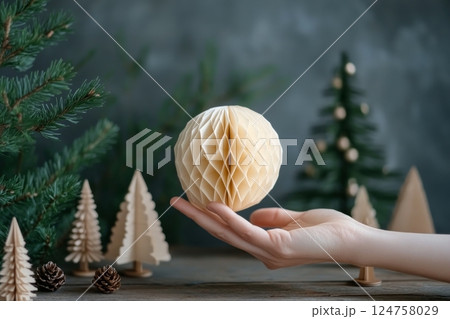 Decorative Paper Globe Held Against a Backdrop of Faux Pine Trees During the Holiday Season 124758029