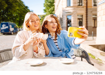 Young women taking selfie while sitting on terrace on sunny day. Girlfriends drink coffee with phone 124758284