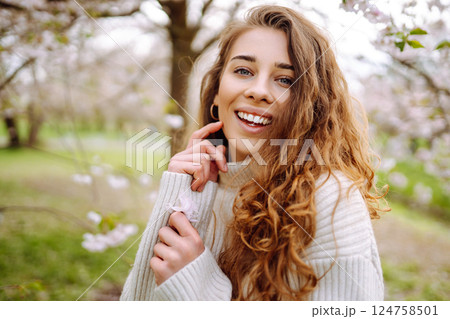 Attractive woman enjoys scent of flowers in spring garden. Concept of relaxation, spring, youth. Attractive woman enjoys scent of flowers in spring garden. Concept of relaxation, spring, youth. 124758501