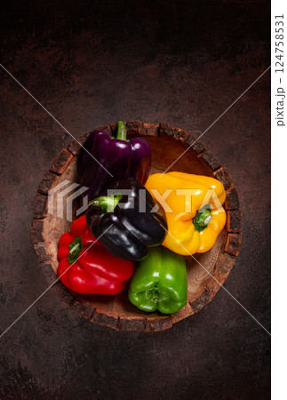 A collection of colorful bell peppers, in a wooden bowl, on a dark surface, top view, no people 124758531