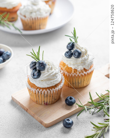 Cupcakes with cream cheese frosting, fresh blueberries and rosemary on a wooden board 124758620